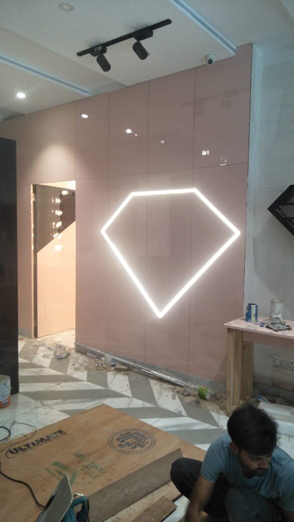 A neon outline of the brand mark on a blush wall, lit, with the floor still being laid.