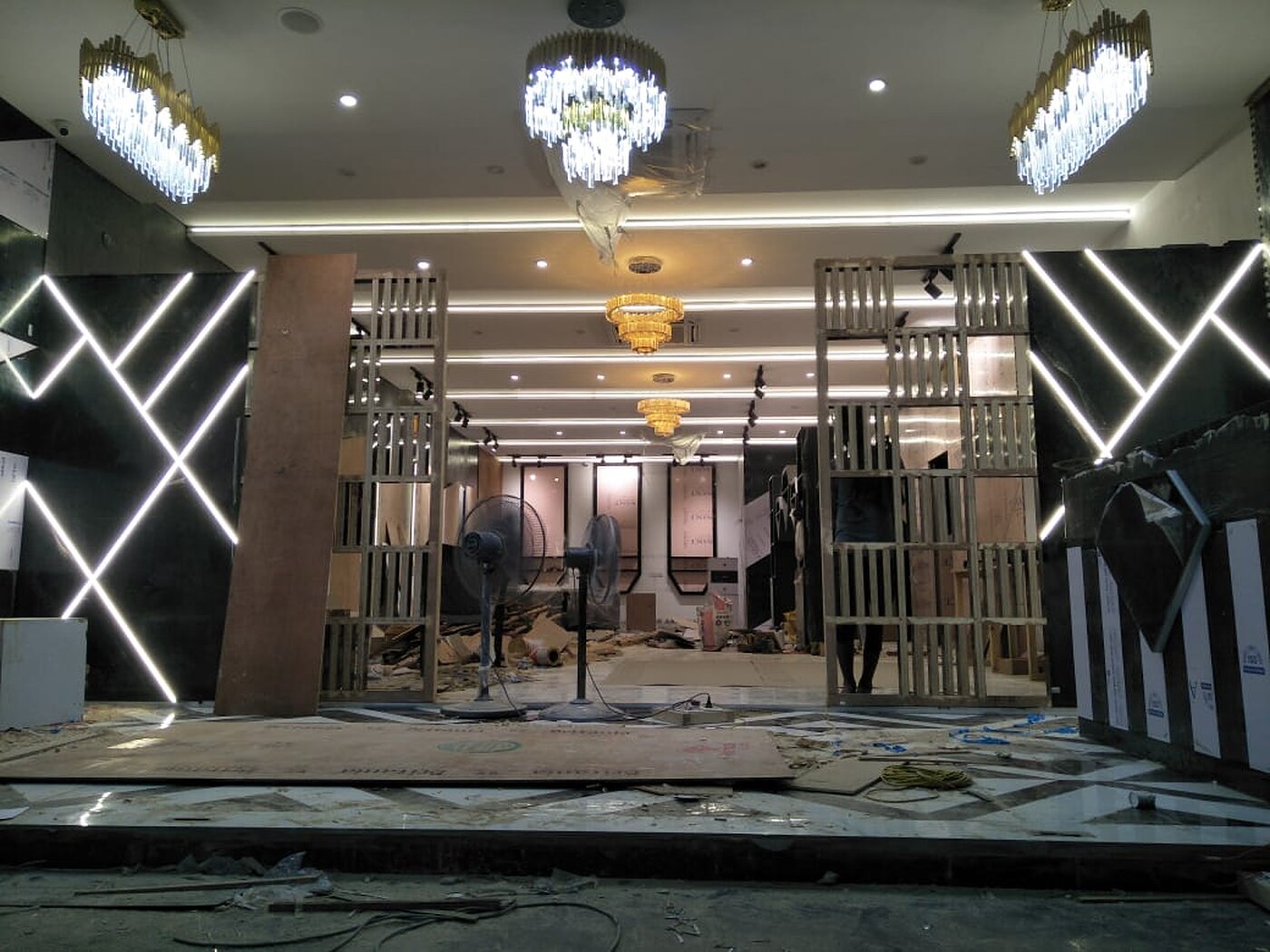 The salon threshold: white neon chevrons cut across black marble either side of a brass fin screen, lit, with crystal chandeliers overhead.