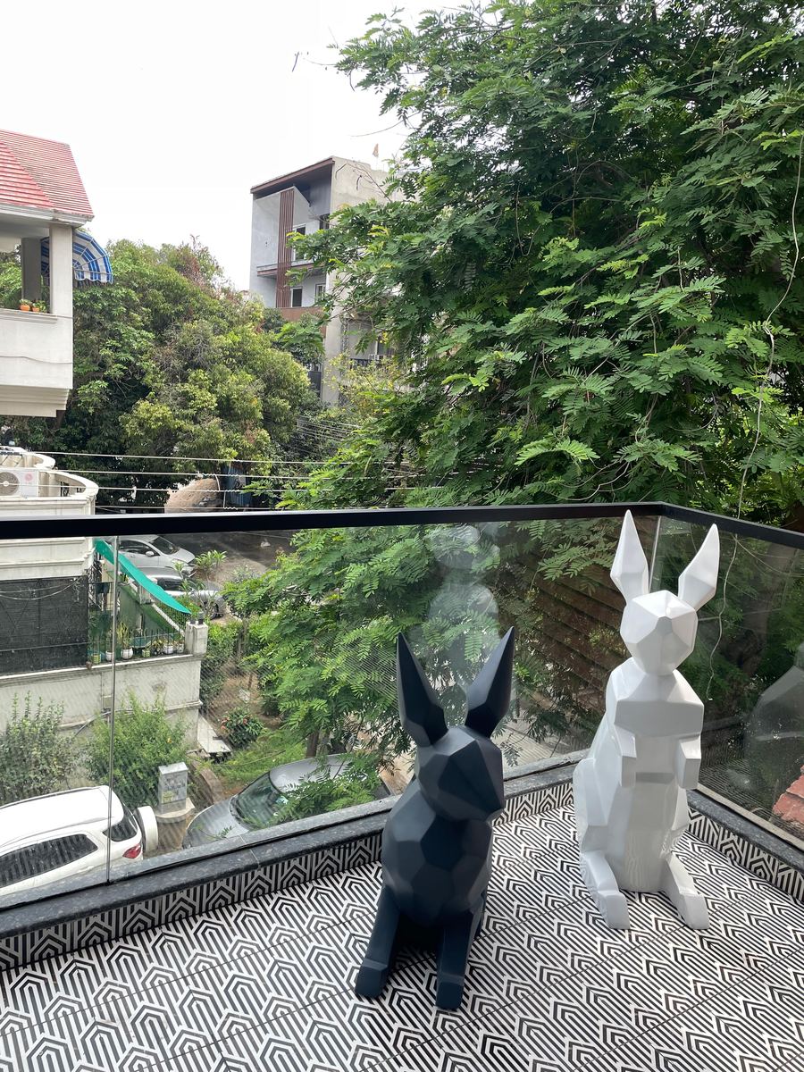 The balcony: two faceted rabbit sculptures on a patterned floor
                  behind a glass balustrade, with the trees of the street beyond.