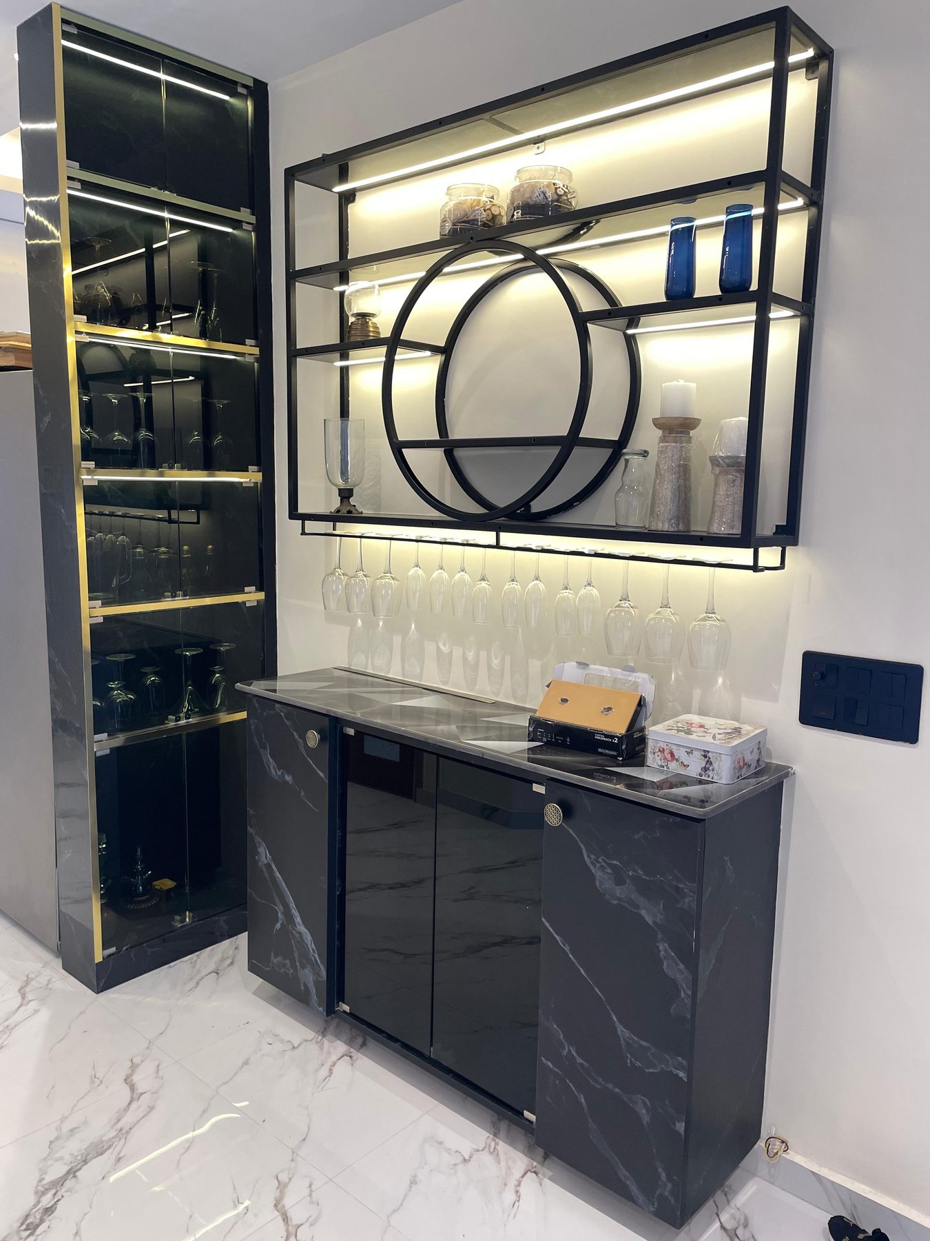The bar close up: the marble counter, the glasses in their rail and
                  the circular motif set into the lit shelving above.