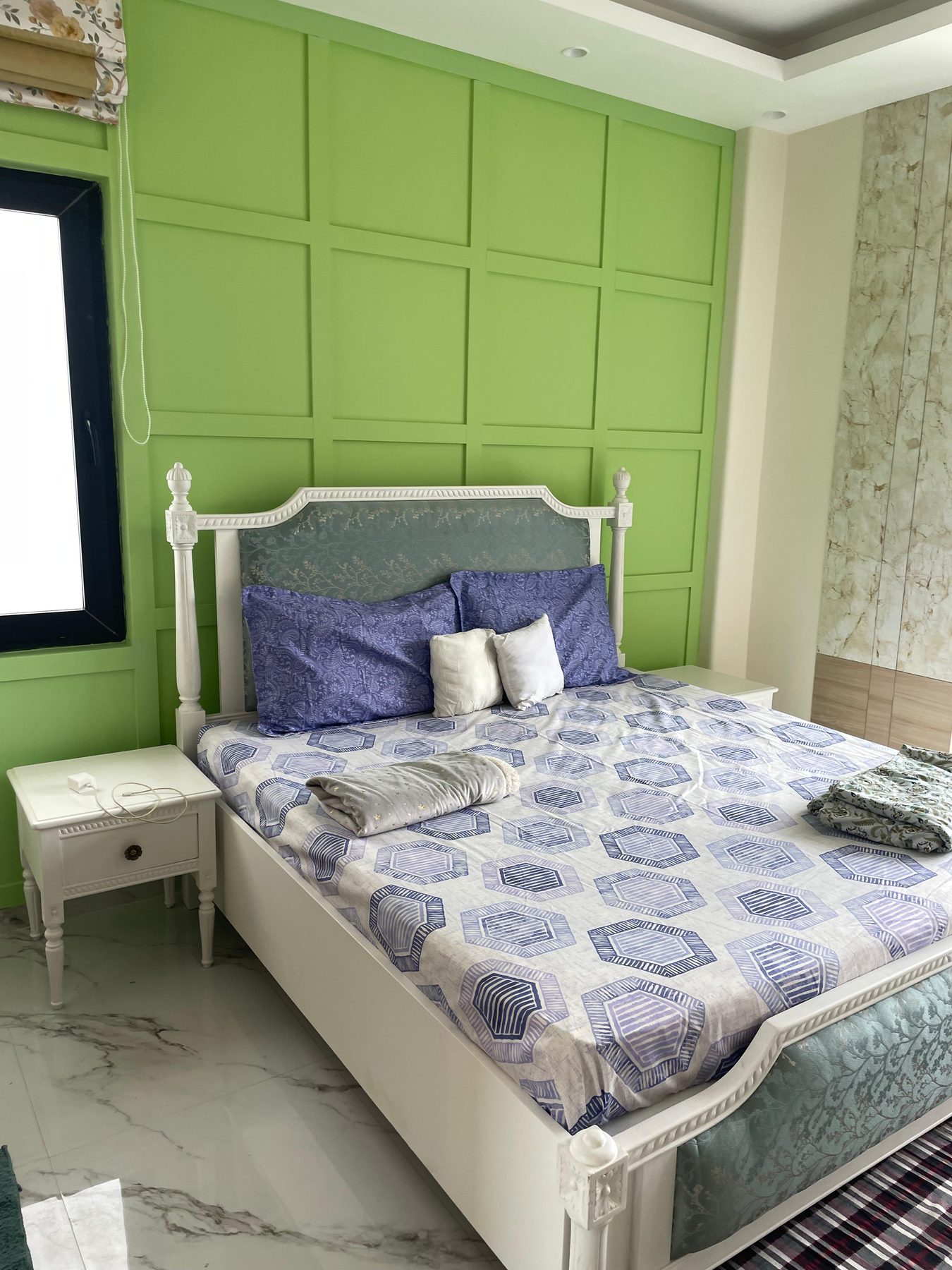 A bedroom finished in green: full-height panelling behind a white
                  bed, patterned bedlinen, a white nightstand and marble underfoot.