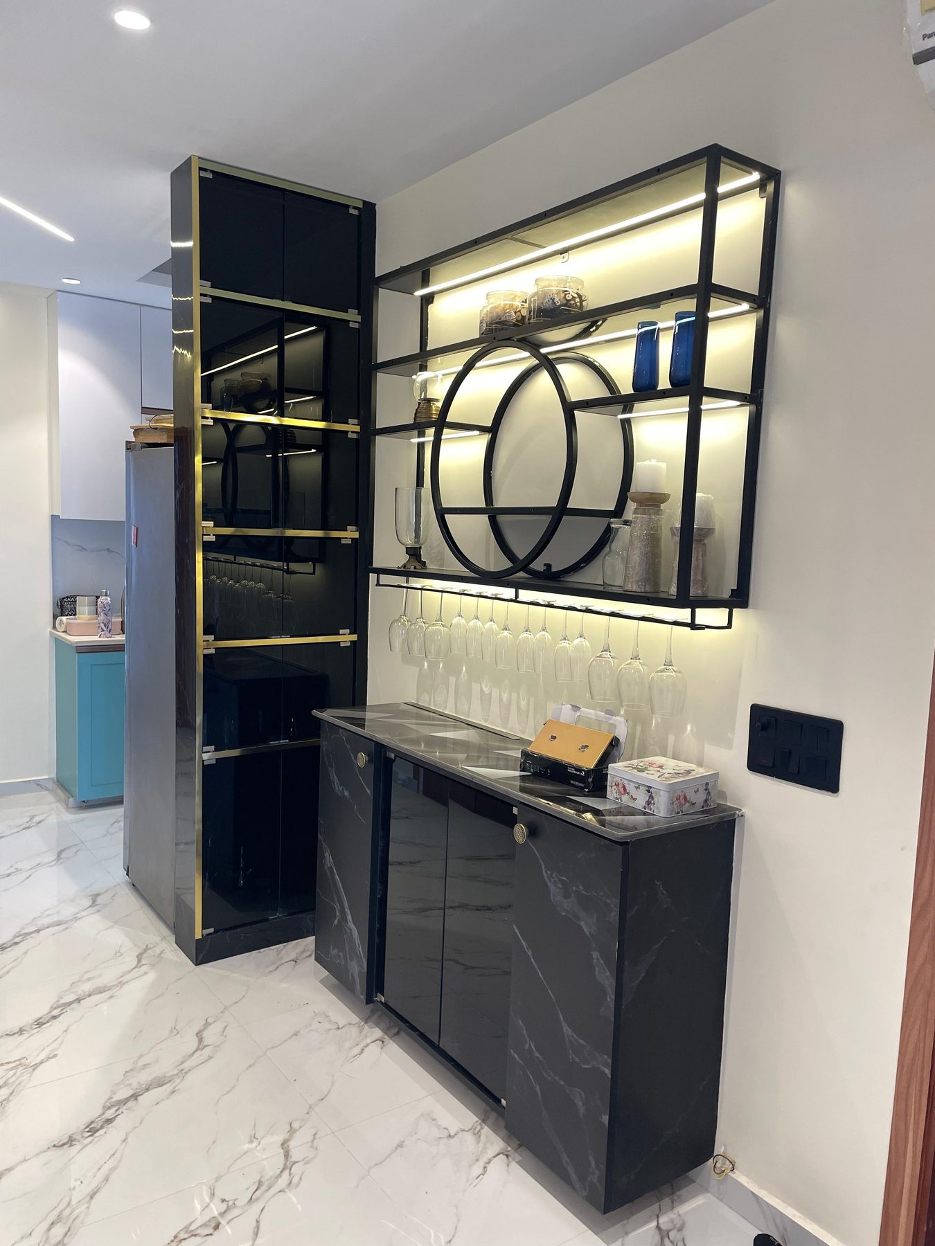 The bar: a dark marble counter below black-framed shelving lit from
                  within, glasses hung under the lowest shelf and a mirrored bottle
                  cabinet alongside.