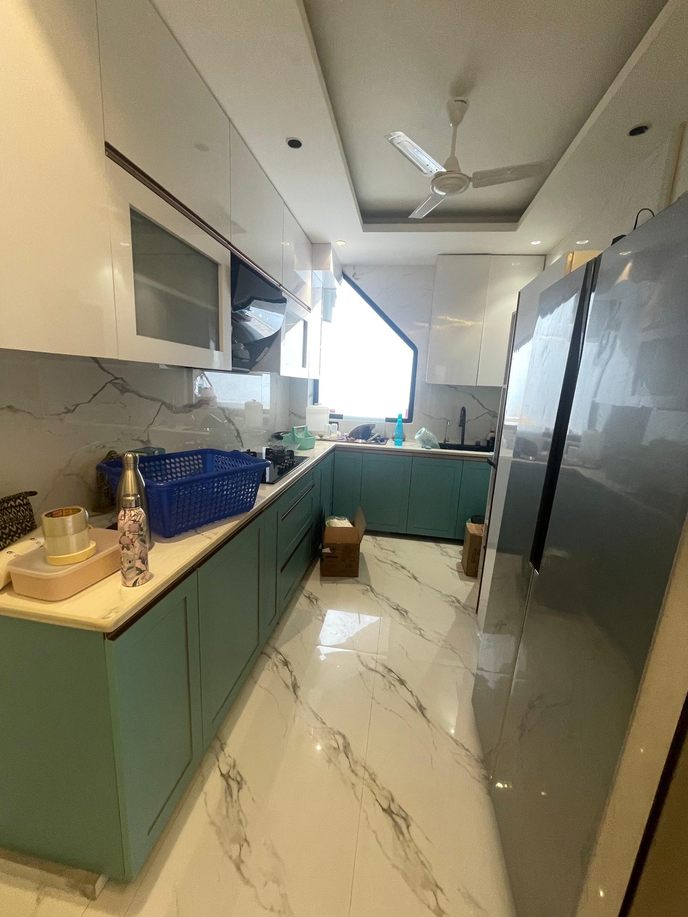 The kitchen as built: sage green base units under a cream counter,
                  white wall cabinets above and a marble floor running to the fridge
                  in the far corner.
