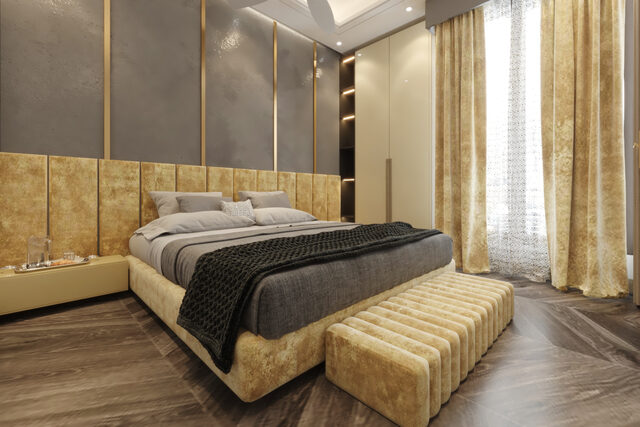 A bedroom with a quilted gold headboard wall, gold curtains and a dark timber floor.