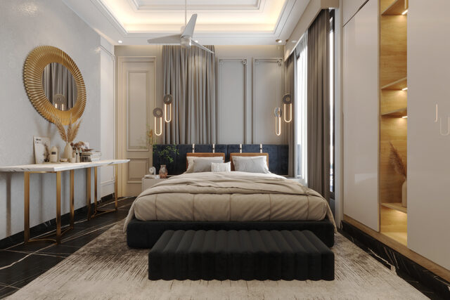 A round gilt mirror over a slim console, beside a dark upholstered bed and fitted wardrobe.
