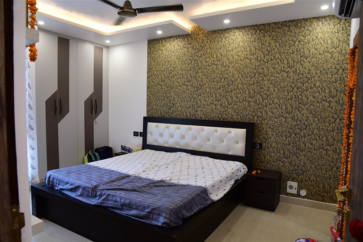 The main bedroom as built, a gold damask feature wall behind a buttoned white headboard, with marigold garlands hung for the housewarming.