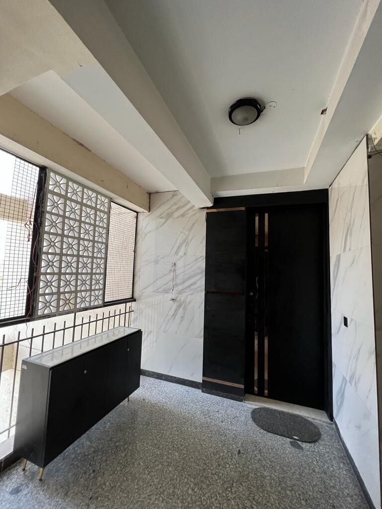 The entrance landing as built: a perforated screen across the window, a
                  marble-veined panel beside the dark timber double door, and a black
                  console standing on terrazzo.