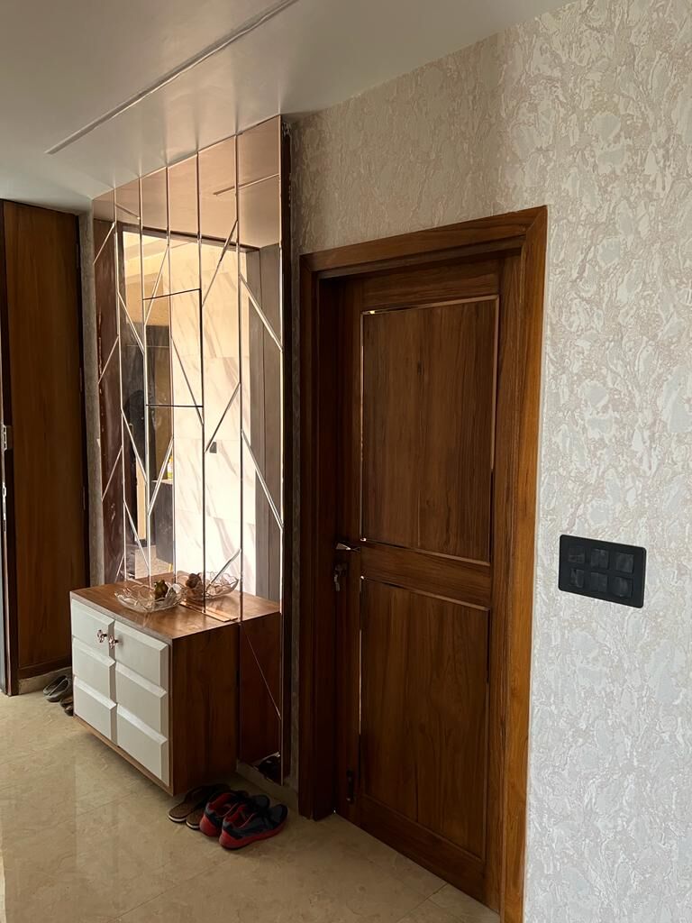 The vestibule inside the door: a mirrored panel held in a slim copper
                  grid, a timber door beside it and a low shoe cabinet beneath.