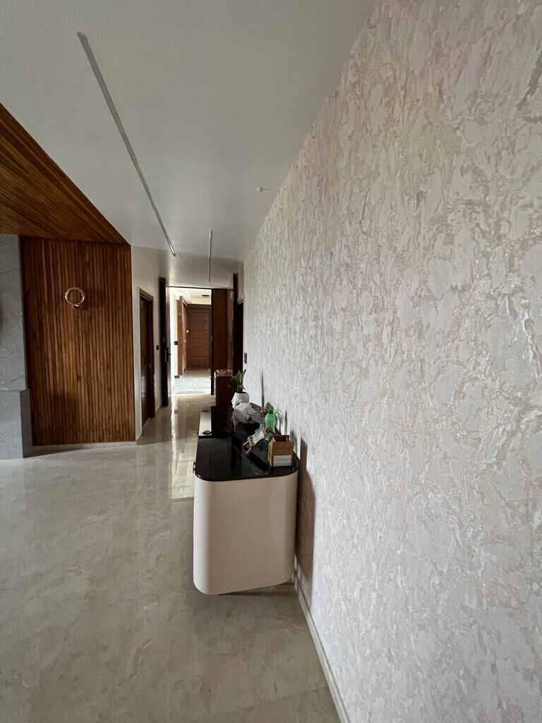 The corridor: a wall of white textured stone, a rounded console carrying
                  a vase, and marble flooring running on past the timber door frames.