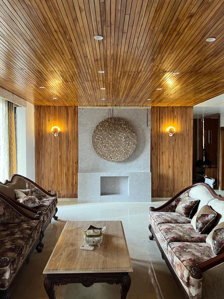 The formal living room head-on: a circular textured medallion set into a
                  stone panel between two wall lights, the timber slat ceiling above and
                  carved sofas facing across a low table.