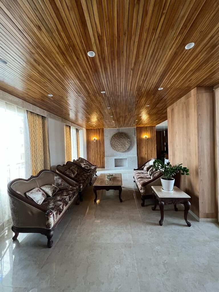 The same room from the window end, the curtained glazing to one side and
                  the sofas in a row down the length of it.