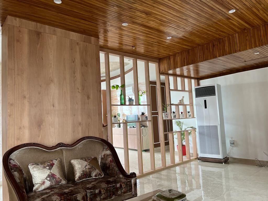 A corner of the living room: a carved sofa against timber panelling, a
                  glazed timber-framed screen with shelving behind it, and marble
                  underfoot.